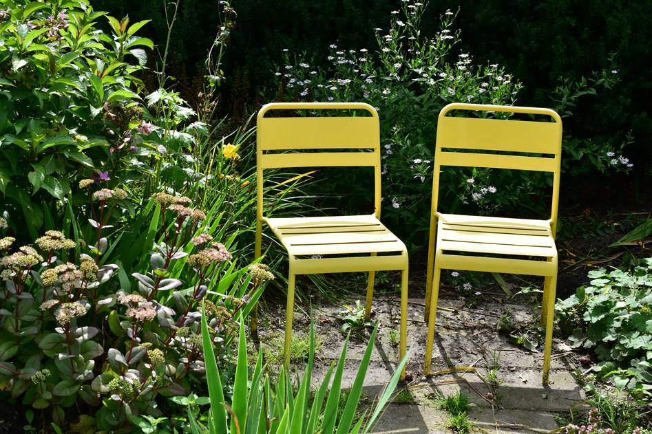 Editor testing a stackable metal garden chair on a grassy lawn with notebook in hand